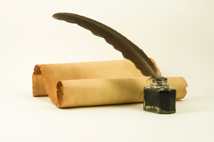 Foto: vergilbte Papierrolle S-förmig gerollt, davor ein Tintenfäßchen aus Glas mit Tinte und einer Feder eingesteckt.
